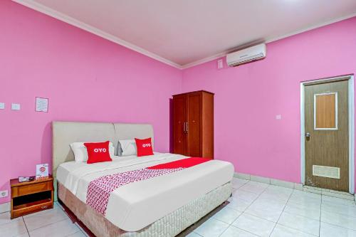 a bedroom with pink walls and a bed with red pillows at OYO 90218 Ubaran Guest House in Bandung