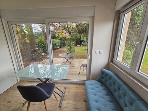 une table en verre et un canapé bleu dans une chambre avec fenêtre dans l'établissement Studio avec terrasse et tonnelle, à Parempuyre