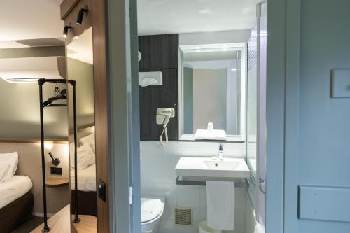een badkamer met een wastafel, een toilet en een spiegel bij Kyriad Nancy Sud - Ludres in Ludres