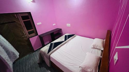 a bedroom with pink walls and a bed with white sheets at Supritha Homestay Hampi in Hampi