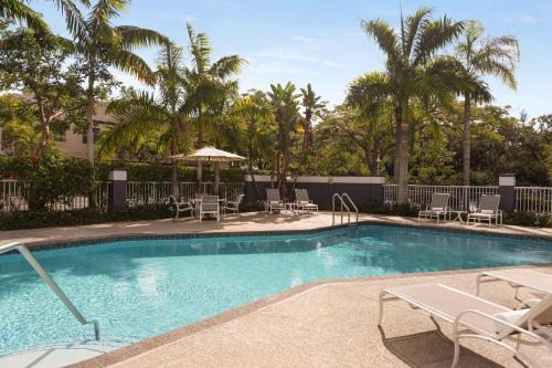a swimming pool with chairs and umbrellas and palm trees at Hampton Inn Pembroke Pines in Pembroke Pines