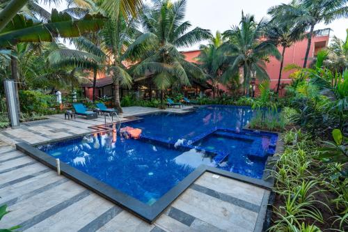 a pool in a resort with blue water and palm trees at Mandrem Beach Resort, a member of Radisson Individuals Retreat in Mandrem
