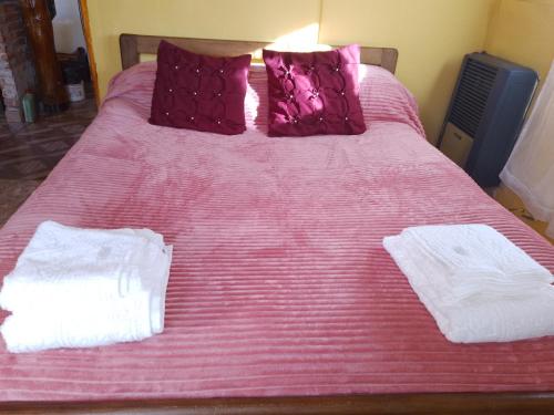 Una cama rosa con dos toallas blancas. en Rinconcito de CHABELA en Junín de los Andes