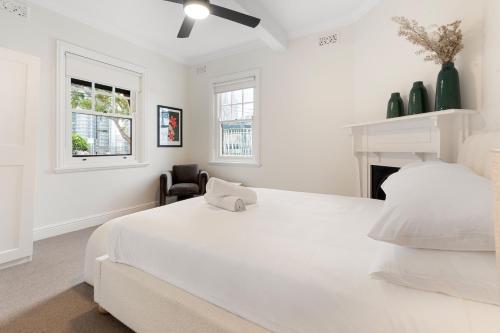 a white bedroom with a white bed and a chair at Heritage Terrace with Harbour Glimpses for 6 in Sydney