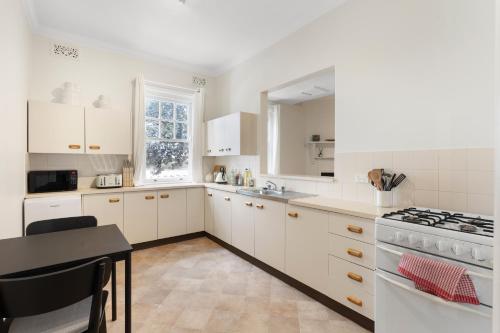 a kitchen with white cabinets and a table and a stove at Heritage Terrace with Harbour Glimpses for 6 in Sydney