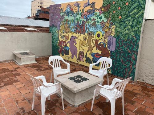 Urban Jungle Hostel في سان ميغيل دي توكومان: مجموعة من الكراسي البيضاء وطاولة أمام جدارية