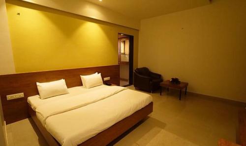 a bedroom with a large white bed and a chair at FabHotel Vovam Service Apartment in Nashik