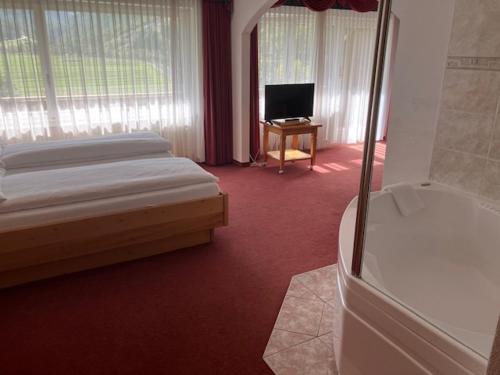 Schlafzimmer mit einem Bett, einem TV und einer Badewanne in der Unterkunft Walliserhof in Täsch