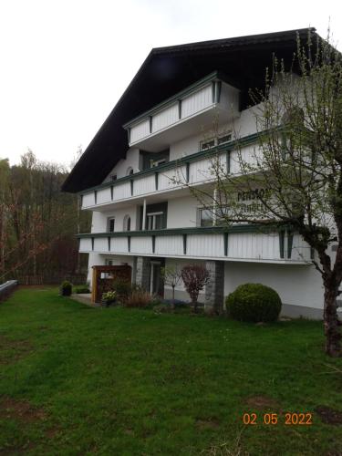a white building with a black roof and a yard at Pension Anderl in Bodenmais