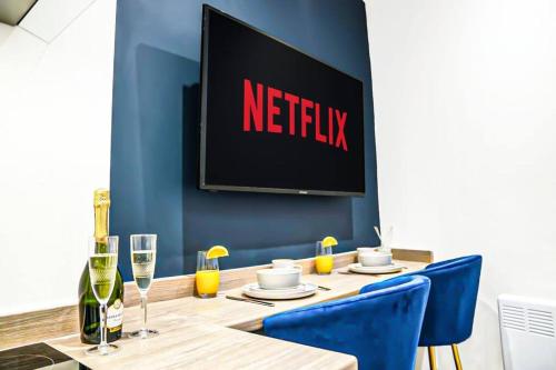 a table with blue chairs and a television on a wall at Luxury City Centre Apartment with Juliet Balcony, Fast Wifi and SmartTV with Netflix by Yoko Property in Aylesbury