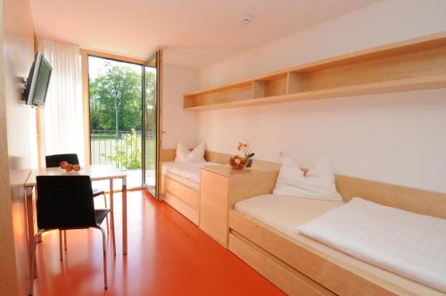a room with two beds and a desk and a table at Olympiazentrum Vorarlberg in Dornbirn