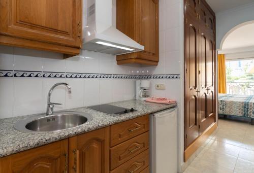 a kitchen with a sink and wooden cabinets at Apartamentos Leonor Carihuela in Torremolinos