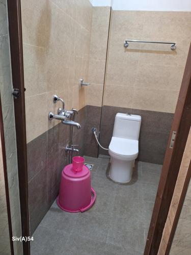 La salle de bains est pourvue de toilettes et d'un seau rose. dans l'établissement Viruksham Residency, à Palni