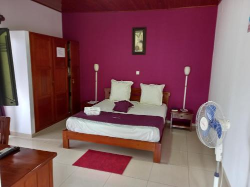 a bedroom with a bed with purple walls and a fan at Hôtel Saïfee International in Toliara