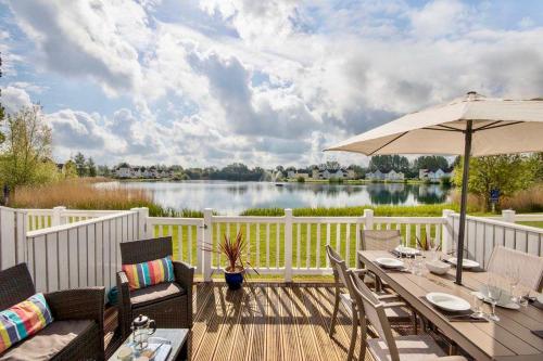 a wooden deck with a table and an umbrella at Spinnaker Lodge · Cotswolds Lakeside Home in South Cerney