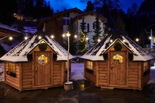 two wooden cabins with snow on the roofs at night at Matthiol Boutique Hotel in Zermatt