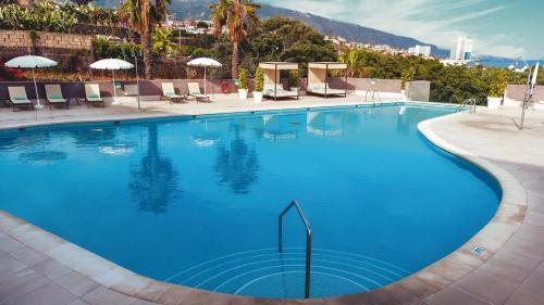 Una gran piscina azul con sillas y sombrillas. en AluaSoul Orotava Valley - Adults Only, en Puerto de la Cruz