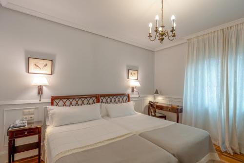 a bedroom with a large white bed and a chandelier at Hotel Alcazar Irun in Irún