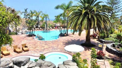 einen Pool mit einer Palme, Stühlen und einem Tisch in der Unterkunft Apartamento AP1 en Playa de Los Roques, en lado de la playa, con piscina in Los Realejos