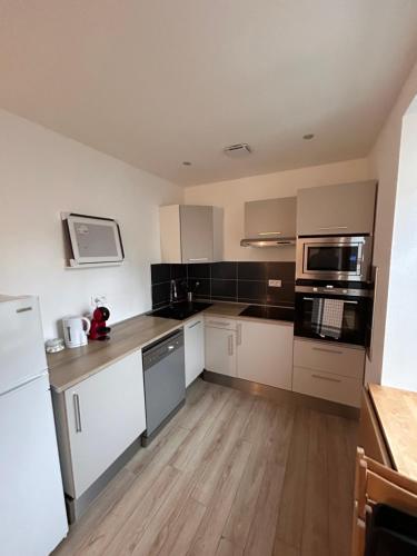 Il comprend une cuisine avec des appareils blancs et noirs et du parquet. dans l'établissement # Le 1 # Très beau T3 Neuf rez-de-chaussée centre ville, à Mulhouse