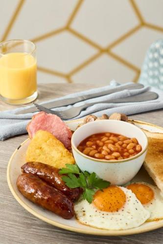 Un plato de desayuno con huevos, salchichas, frijoles y tostadas. en The Essex Golf & Country Club Hotel, en Coggeshall