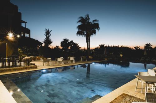 a swimming pool with chairs and a palm tree at Paradis Plage Surf Yoga & Spa in Taghazout