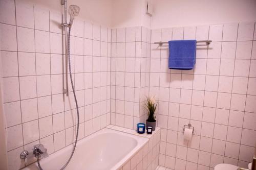 a white tiled bathroom with a tub and a blue towel at Stilvolles Apartment - Messe Rü Innenstadt in Essen
