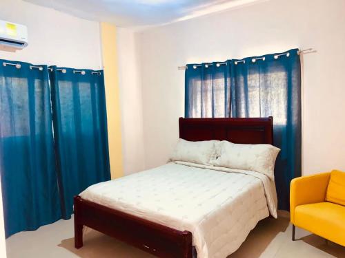 a bedroom with blue curtains and a bed and a yellow chair at Grande y acogedor apartamento cerca de la playa. in Azua de Compostela