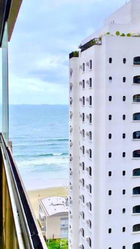 biały budynek obok plaży z oceanem w obiekcie Apartamento a 100m. da Praia de Pitangueiras w mieście Guarujá
