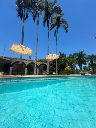einen Pool mit 2 Sonnenschirmen und Palmen in der Unterkunft Villa Aratoca suíte presidencial in Garça