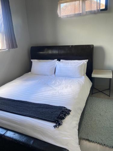 a bed with a black headboard and white sheets and pillows at Pule's Home in Maseru