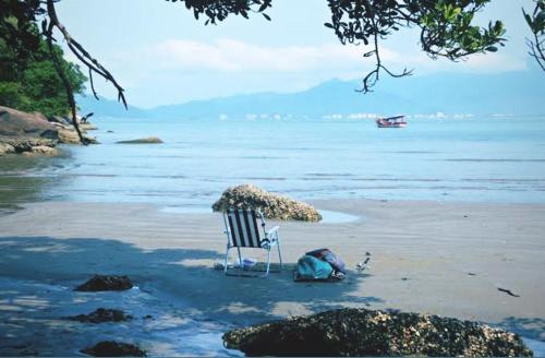 a chair on a beach with a person laying on it at Casa de Praia Beira Mar Bali Beach House in Bertioga
