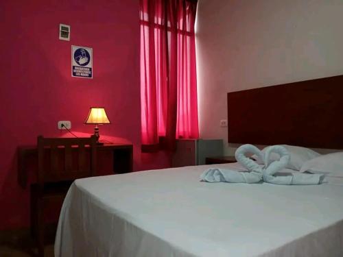 a bedroom with a bed with white sheets and red walls at Hostal Camu Camu in Iquitos