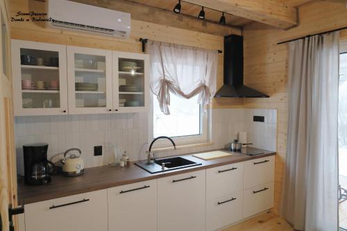 a kitchen with white cabinets and a window at SzumiPuszcza - domki, sauna, balia in Białowieża