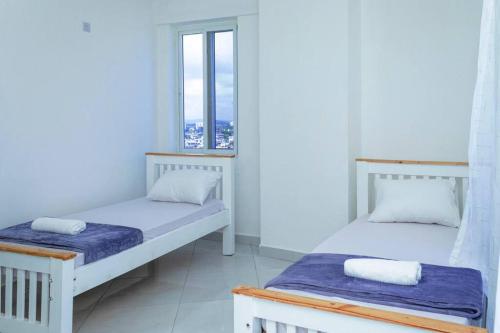Dos camas en una habitación con dos ventanas. en Angani Apartment, AC Installed, Ocean View & Rooftop Pool, en Mombasa