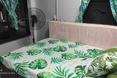 a bed with a green and white comforter and a fan at Baloy beach house in Olongapo