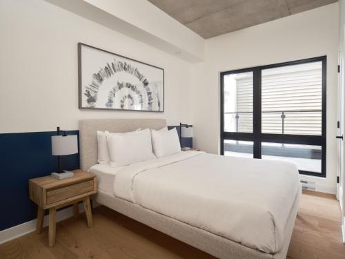 a white bedroom with a large bed and a window at Hôtel Expérience - Quartier Des Marinas in Magog-Orford