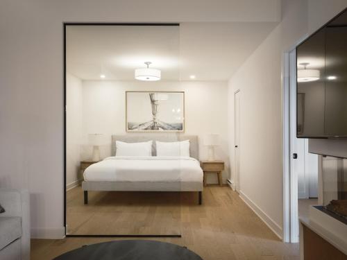 a bedroom with a white bed and a mirror at Hôtel Expérience - Quartier Des Marinas in Magog-Orford