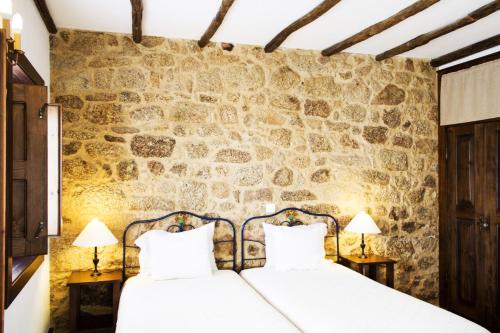 a bedroom with two beds and a stone wall at Casa d'Acha in São Miguel de Acha