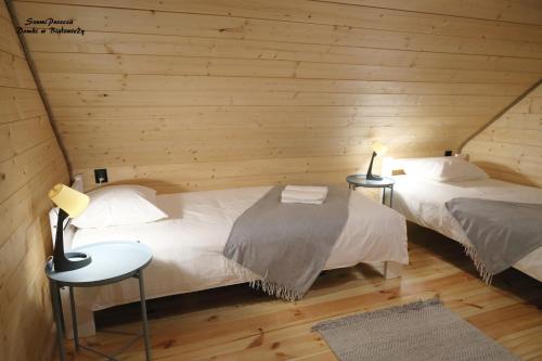 two beds in a room with wooden walls at SzumiPuszcza - domki, sauna, balia in Białowieża