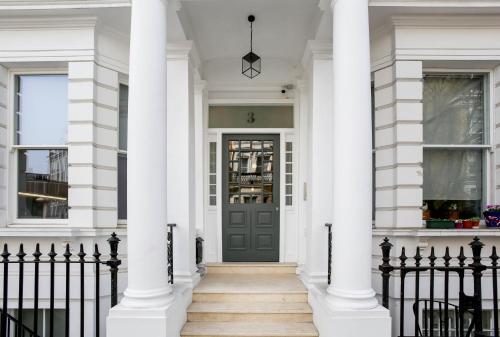 una casa bianca con una porta nera e colonne di Cromwell Serviced Apartments by StayPrime a Londra