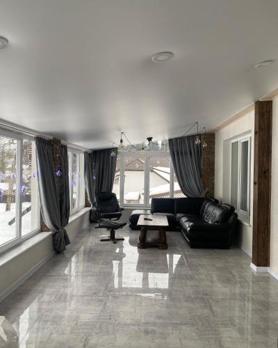 a living room with black leather furniture and large windows at Котедж Смерекова хата- Пилипець in Kelechin