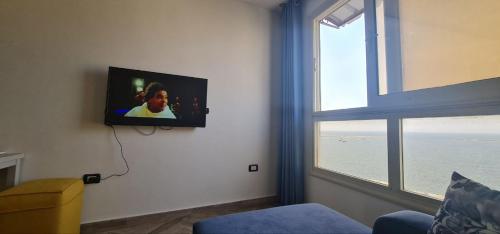 sala de estar con TV en la pared y ventana en شقة فاخرة مكيفة تري البحر مباشرة, en Alejandría