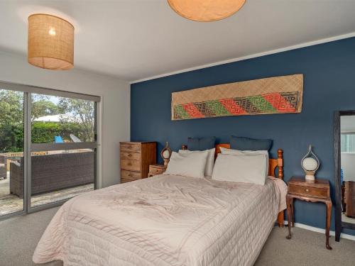 Un dormitorio con una cama con paredes azules y una ventana en Kon Tiki Retreat - Whiritoa Beach Holiday Home en Whiritoa