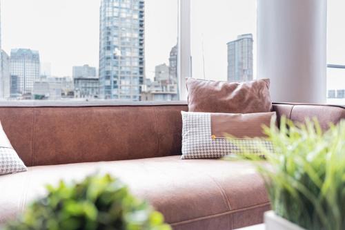 a brown couch in a room with a large window at Near BC Place & SkyTrain Access & Free Parking in Vancouver