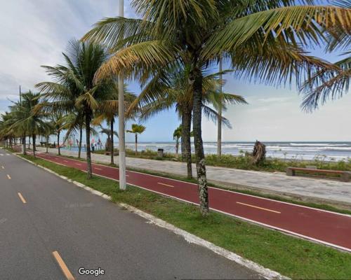 a road with palm trees on the side of a beach at Aconchegante casa a 50m da praia in Praia Grande