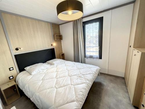 une chambre avec un lit blanc et une grande fenêtre dans l'établissement Chalet cosy 4 pers - Piscine chauffée - Proche plage et commerces - Terrasse et jardin privés - FR-1-361-504, à Jullouville