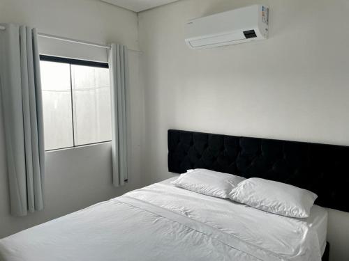 a white bed with a black headboard and a window at Unidades mobiliadas em condomínio in Lucas do Rio Verde