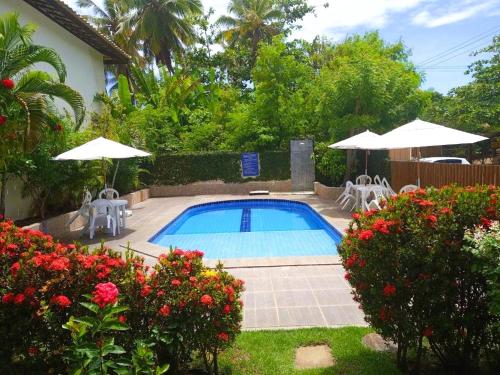 a swimming pool with two umbrellas and some flowers at Residence Cotê d' Azur in Imbassai