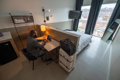 a man sitting at a desk with a laptop in a bedroom at Arch + Cable Hotel in Mankato
